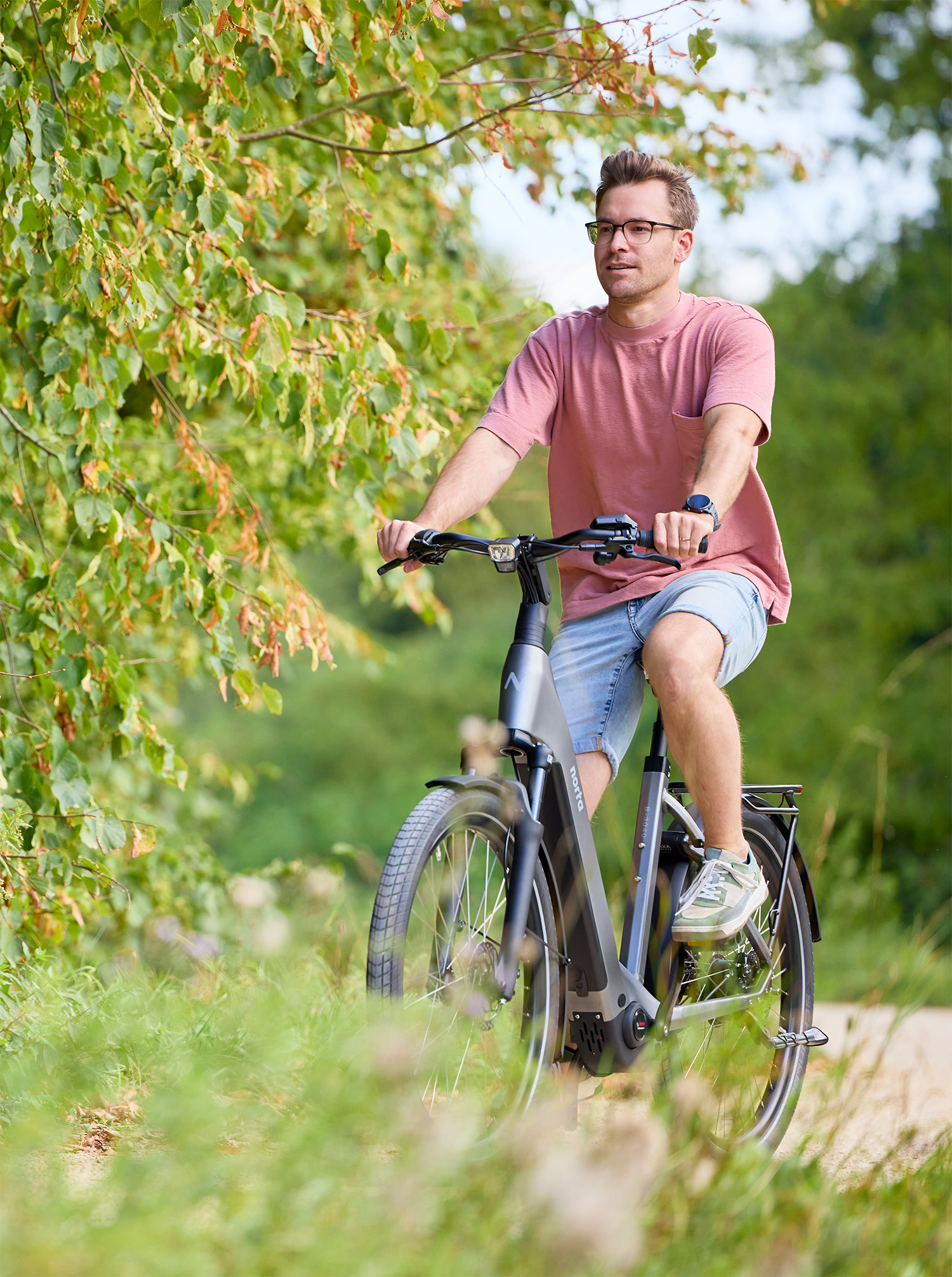 Man fietst op een grijze/gun metal elektrische fietsen door een park.