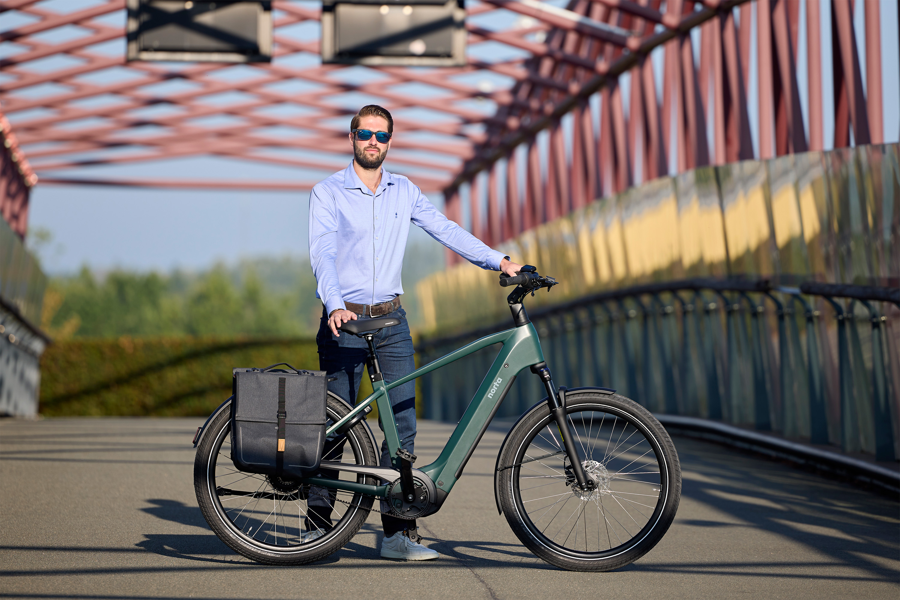 Man staat achter zijn elektrische fiets van Norta. Hij staat achter zijn fiets op een brug. 